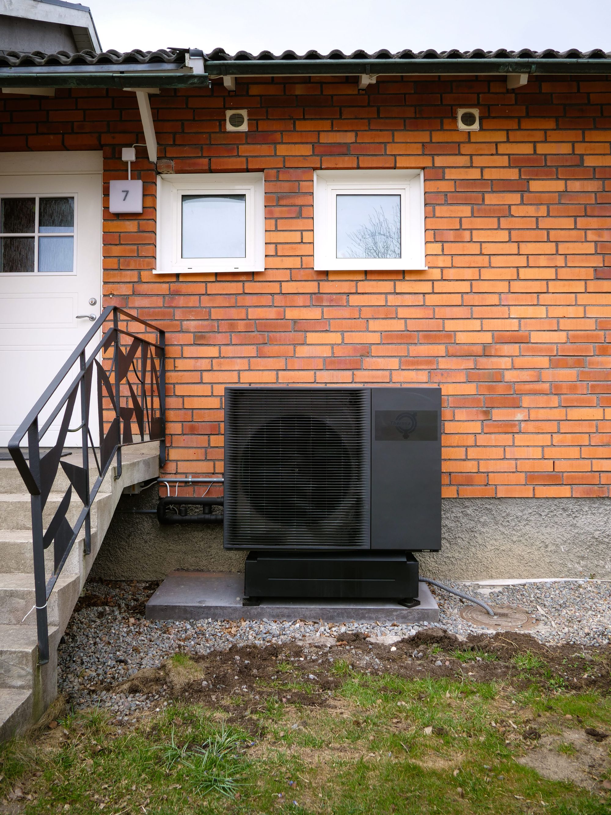 Svart Themial luft vatten värmepump mot husets fasad i Kungsängen